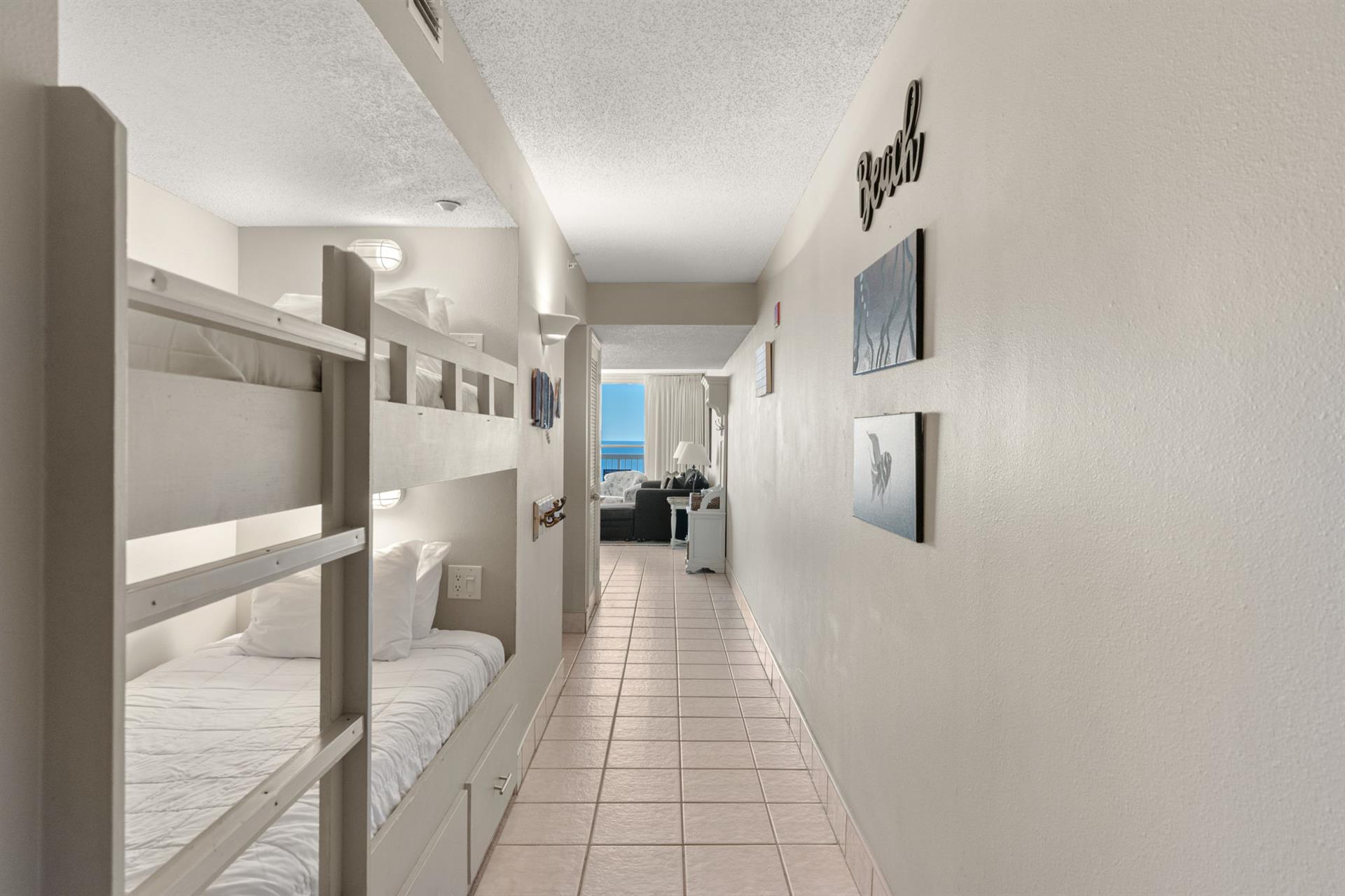 The bunk bed hallway leads to a stunning waterfront living space with glimpses of blue waters ahead.