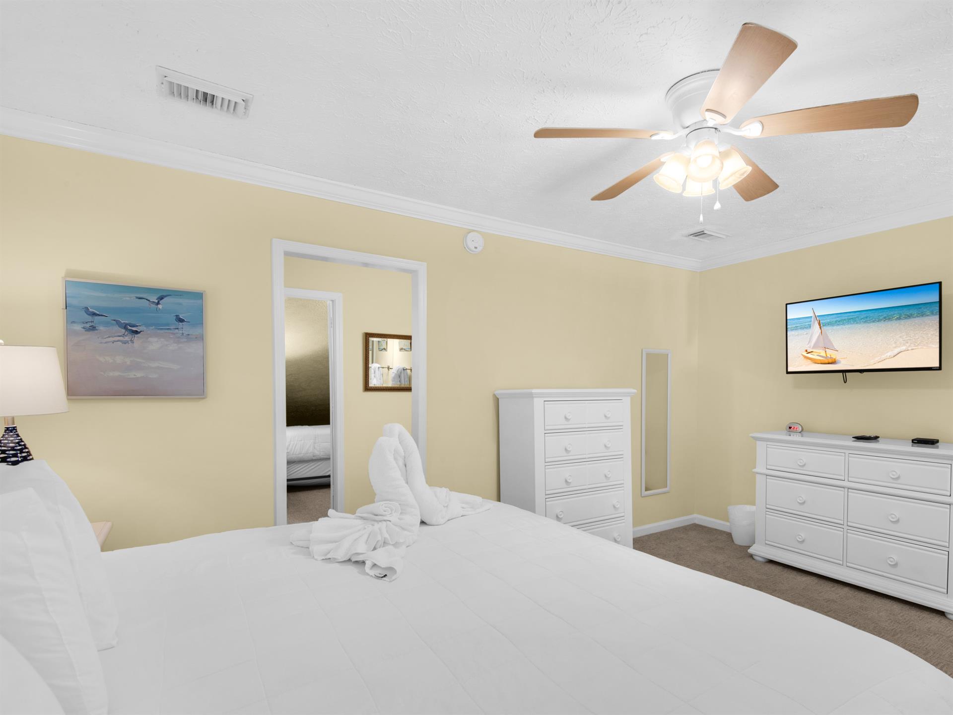 Relax in your peaceful bedroom with crisp white linens, ceiling fan, and calming coastal artwork creating the perfect retreat.