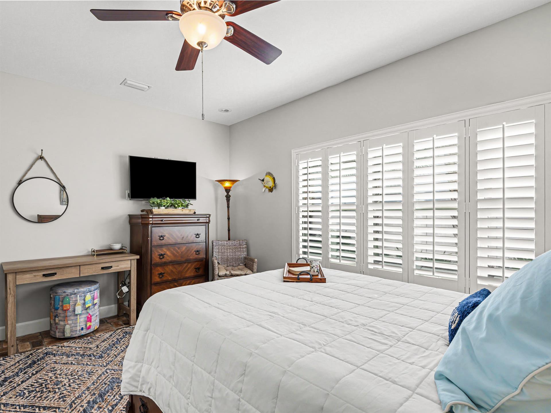 Unwind in your serene bedroom where coastal breezes flow through plantation shutters and a ceiling fan keeps you cool.