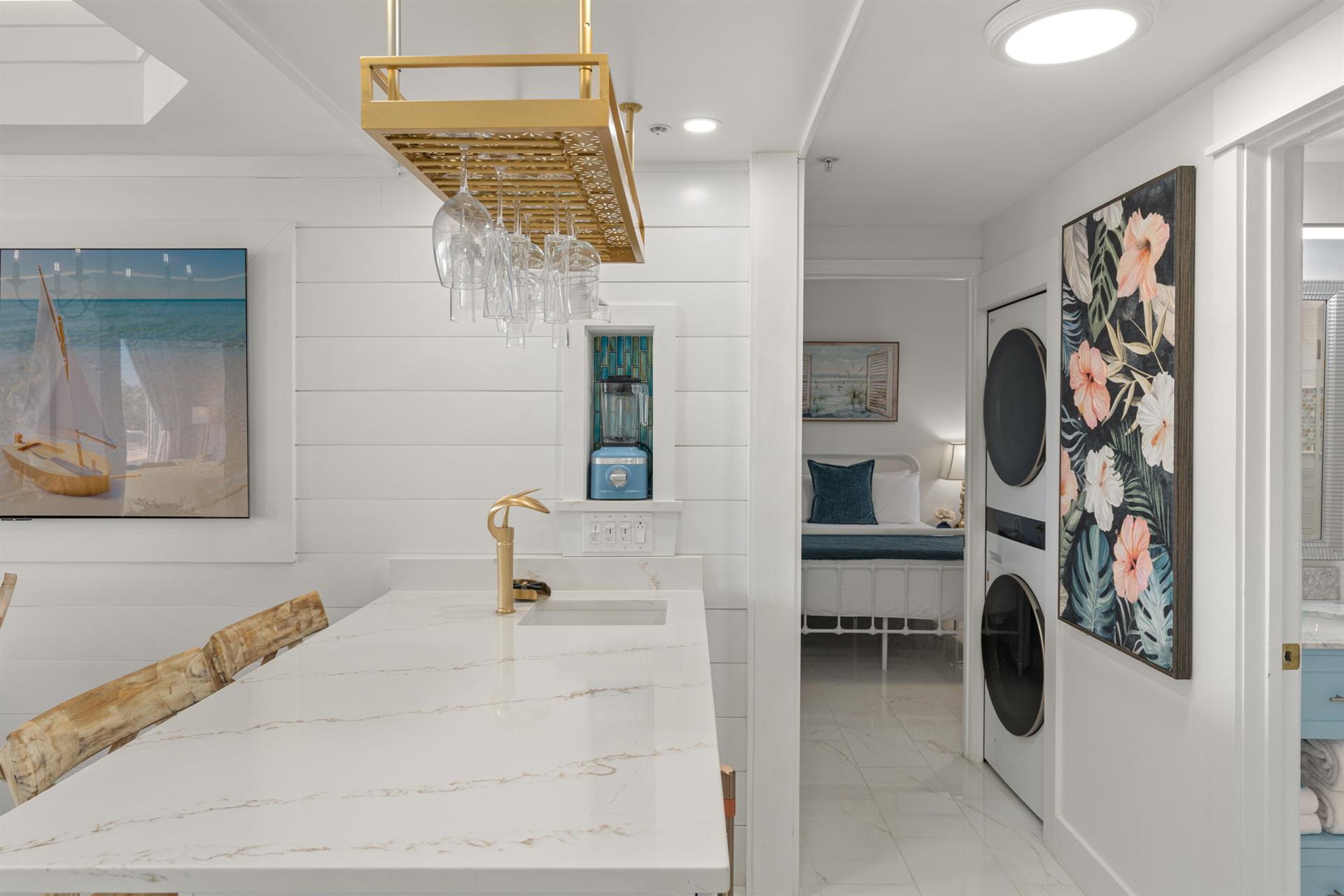 Your stylish kitchen flows seamlessly into a convenient laundry area, where marble counters and coastal artwork create an elegant workspace for cooking and cleaning.