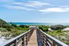 Wooden boardwalk leads through coastal dunes to pristine turquoise waters and sandy beach beyond.