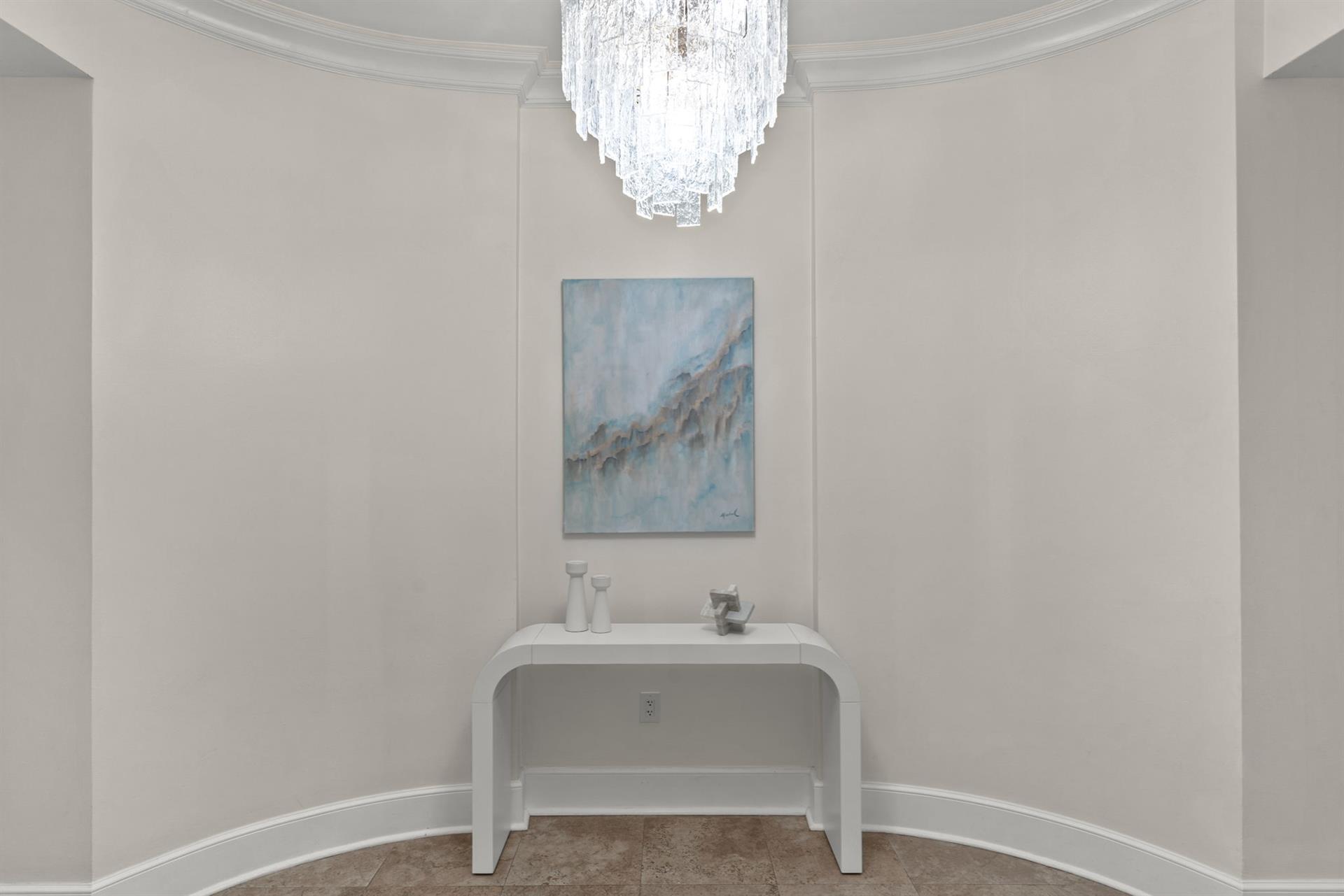 Your elegant foyer welcomes you with a stunning crystal chandelier casting warm light over a sleek console table beneath beautiful artwork.