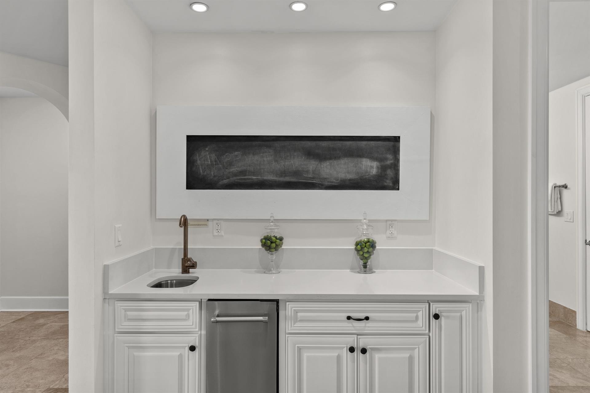 Your private wet bar awaits with elegant white cabinetry, pristine countertops, and stylish artwork—perfect for evening cocktails or morning coffee.