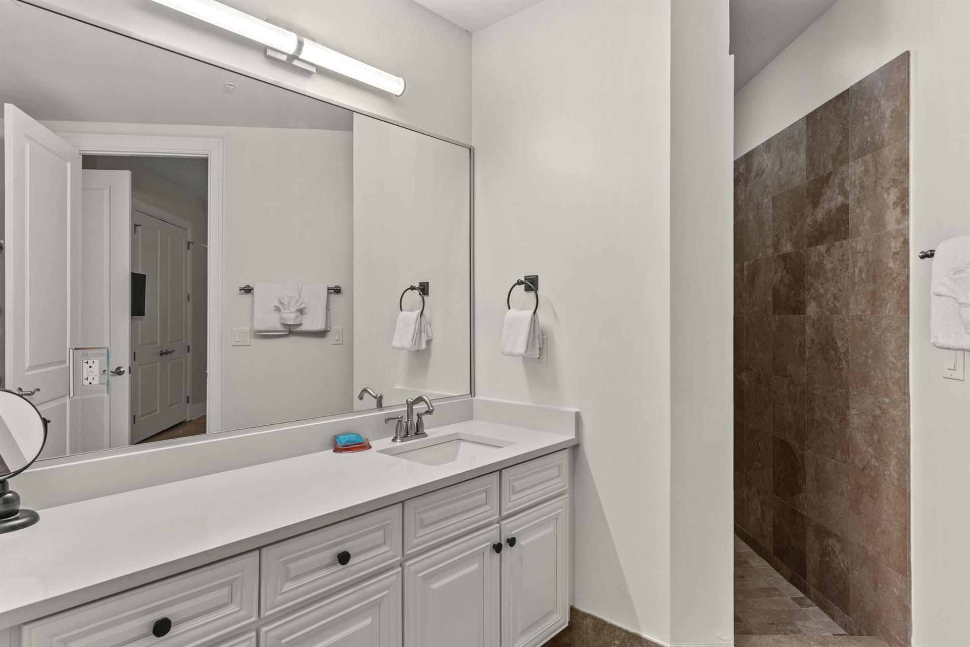 Step into your pristine private bathroom with elegant vanity, generous counter space, and spainspired walkin shower featuring rich stone tile.
