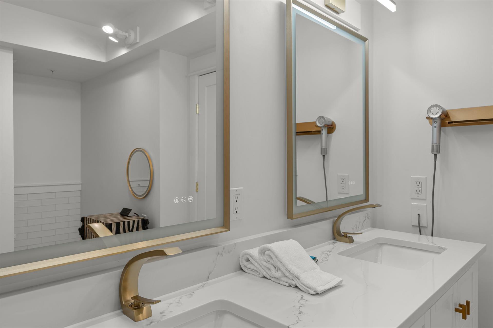 Your elegant bathroom features dual vanities with marble countertops, gold fixtures, and modern mirrors—perfect for refreshing mornings.