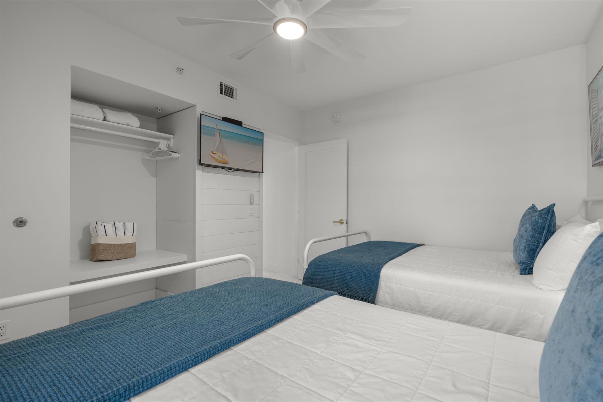 Your coastalthemed bedroom features twin beds with ocean blue accents, ceiling fan for comfort, and TV for relaxation.