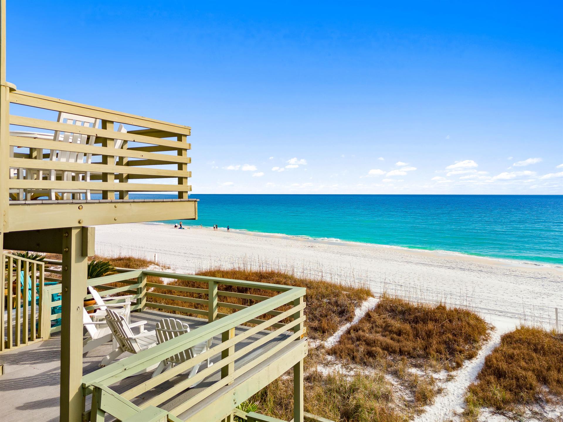 Elevated wooden deck with beach access overlooks pristine white sand and turquoise waters under endless blue sky.