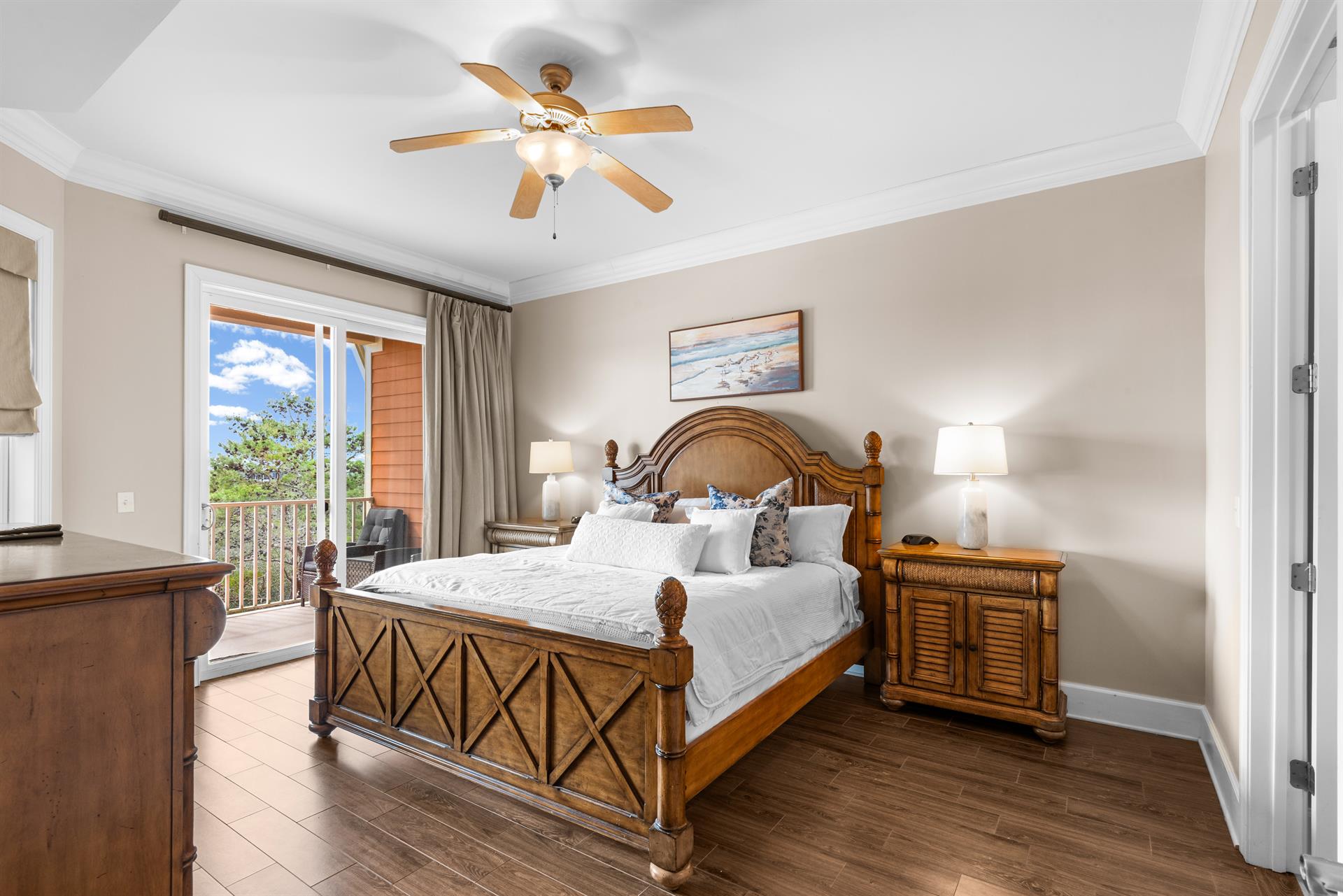 First floor king bedroom with tropical wood furnishings, ceiling fan, and private balcony overlooking lush landscaping.