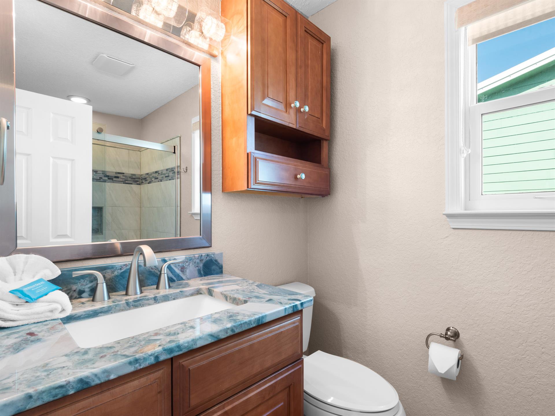Refresh in the elegant primary bathroom featuring beautiful blue marble countertops, warm wood cabinetry, and a luxurious walkin shower.