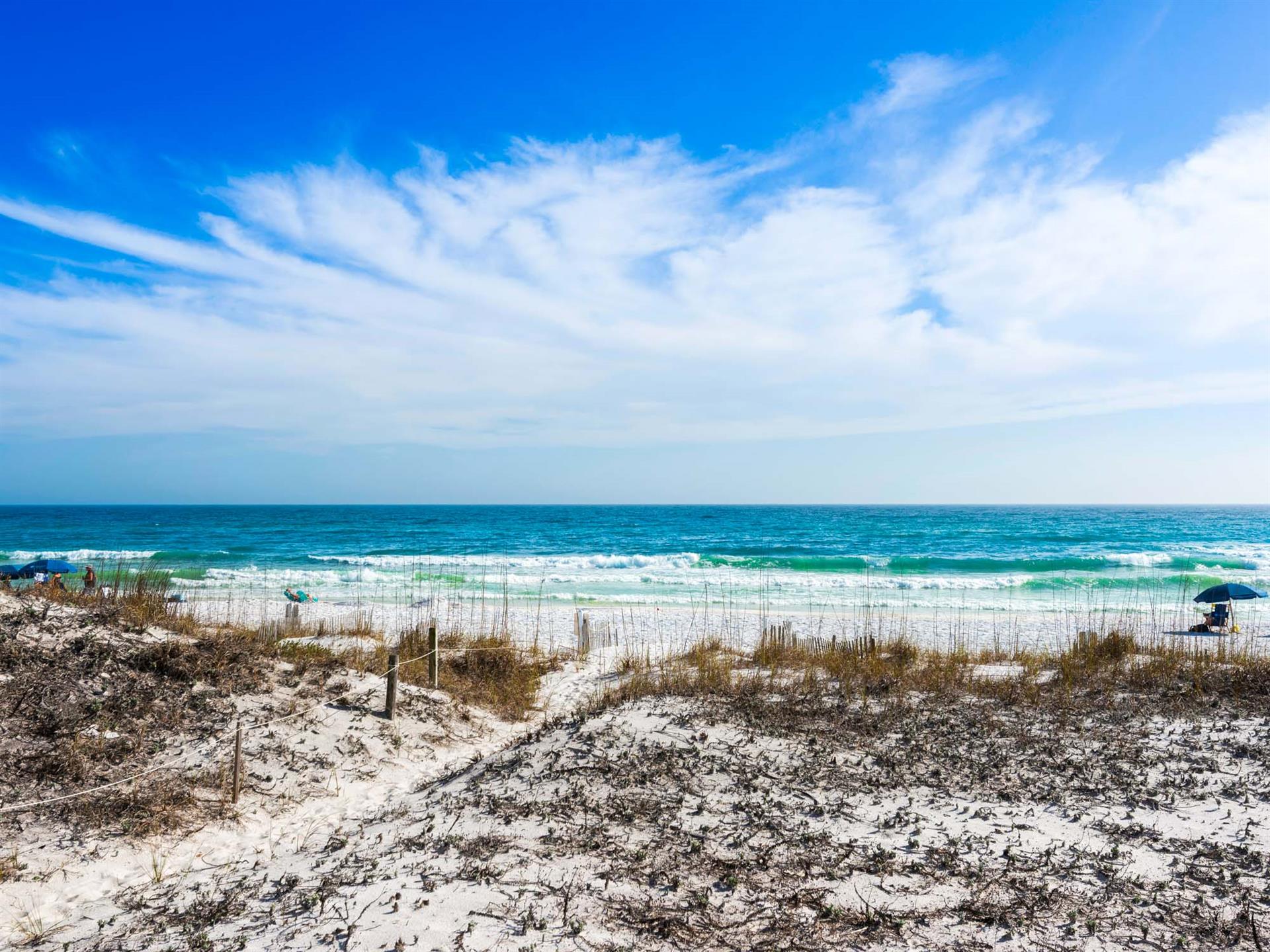 Beautiful beachfront location with pristine white sand, rolling waves, and dramatic blue skies stretching to the horizon.