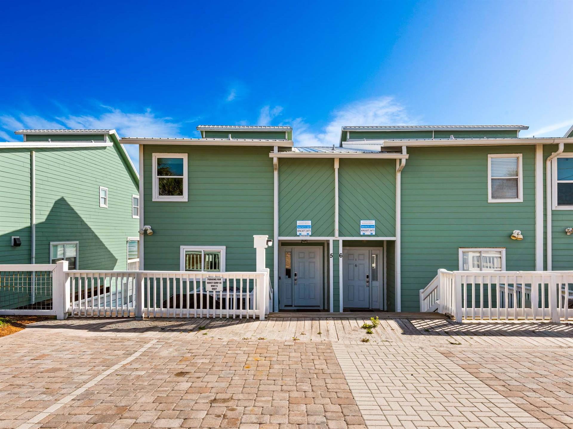Unique townhome complex with charming green siding and white trim under brilliant blue skies.
