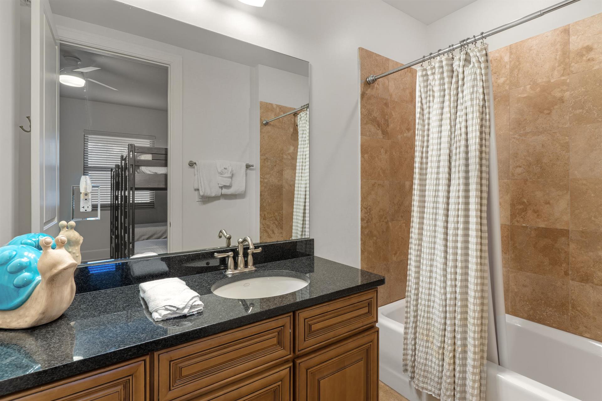 Private bathroom with granite countertops, warm wood cabinetry, and a luxurious tiled showertub combo.