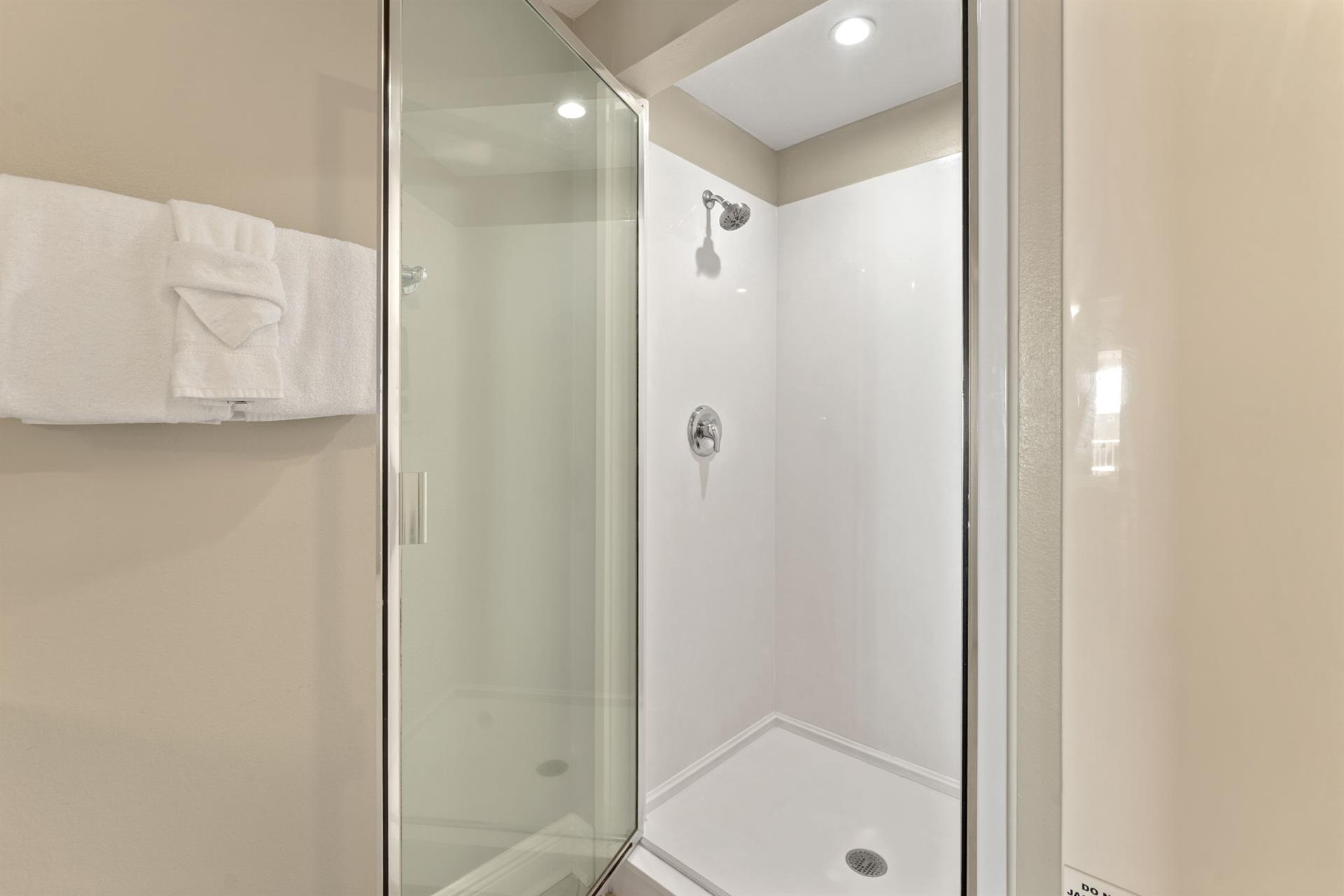 Step into the private glassenclosed shower with fresh white tiles and plush towels ready for your comfort.