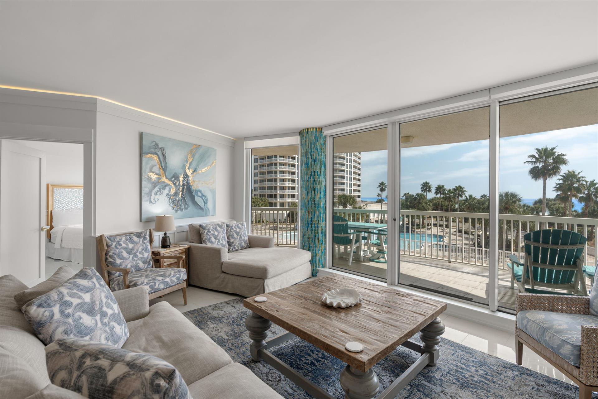 Unwind in your elegant living space with panoramic windows framing tropical palms and azure pools below.