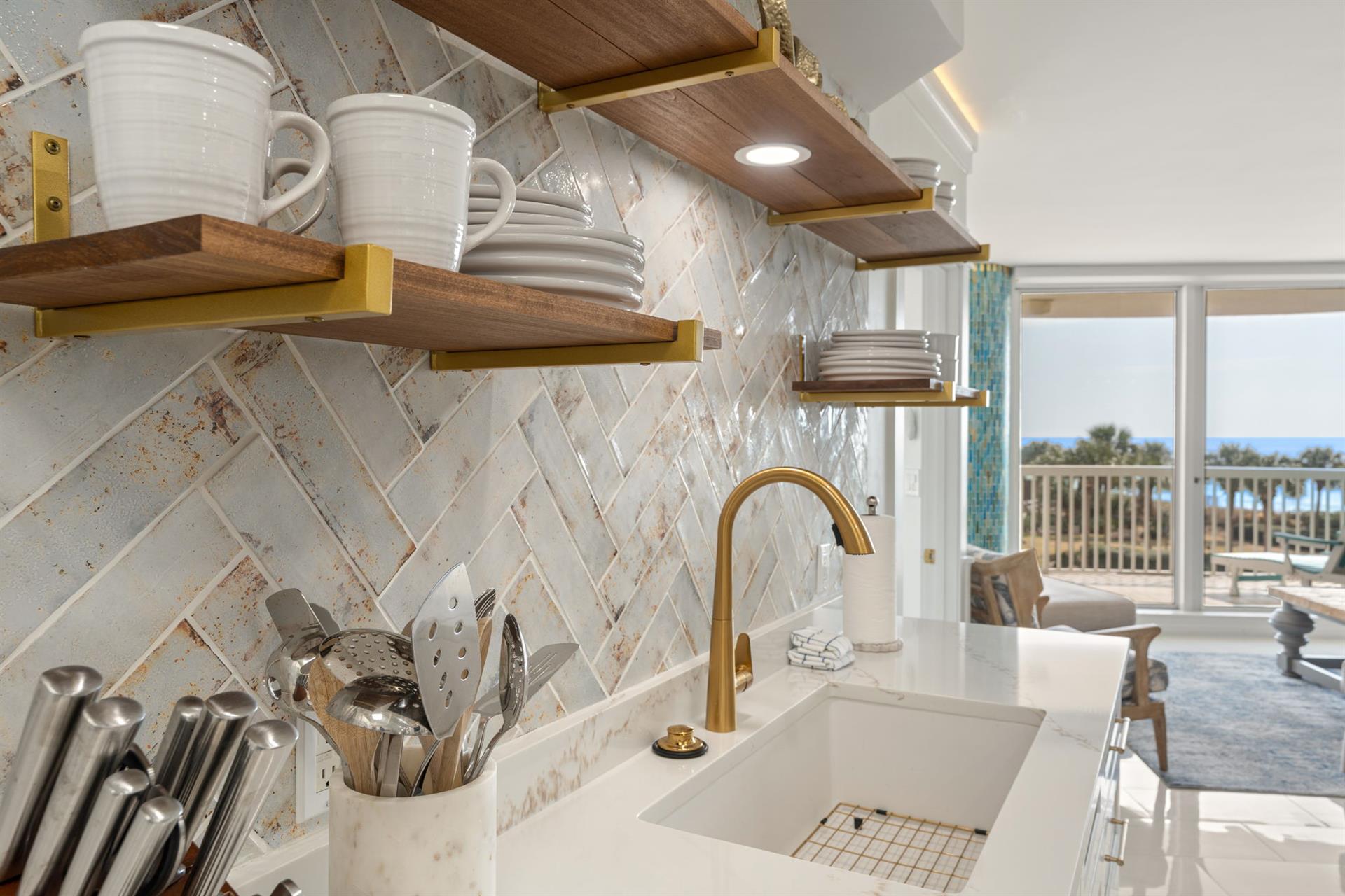 Your stylish kitchen features elegant herringbone backsplash, brass fixtures, and floating shelves with stunning Gulf views.