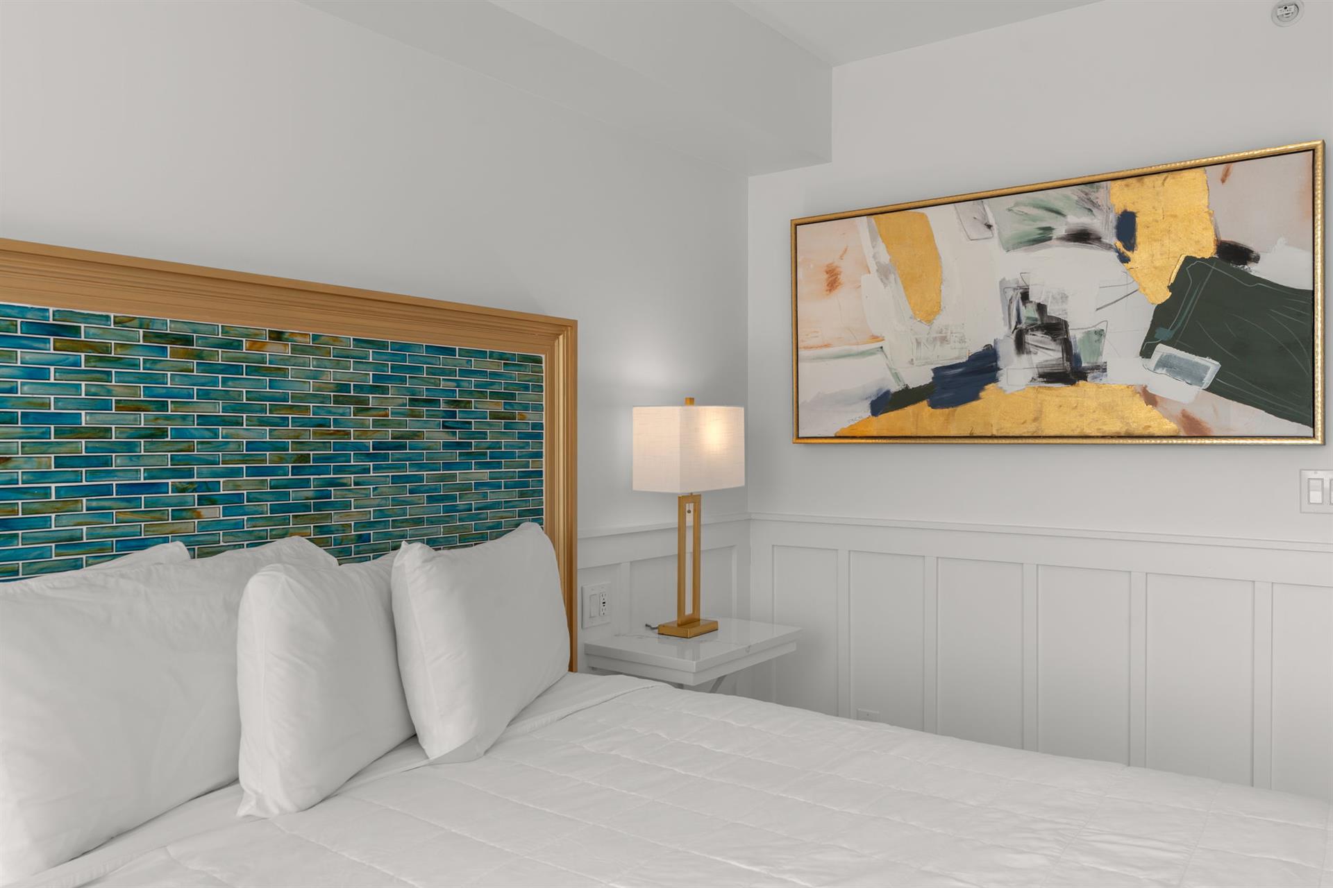 Sink into crisp white linens beneath the stunning teal mosaic headboard, where coastal charm meets modern artistry in your serene retreat.