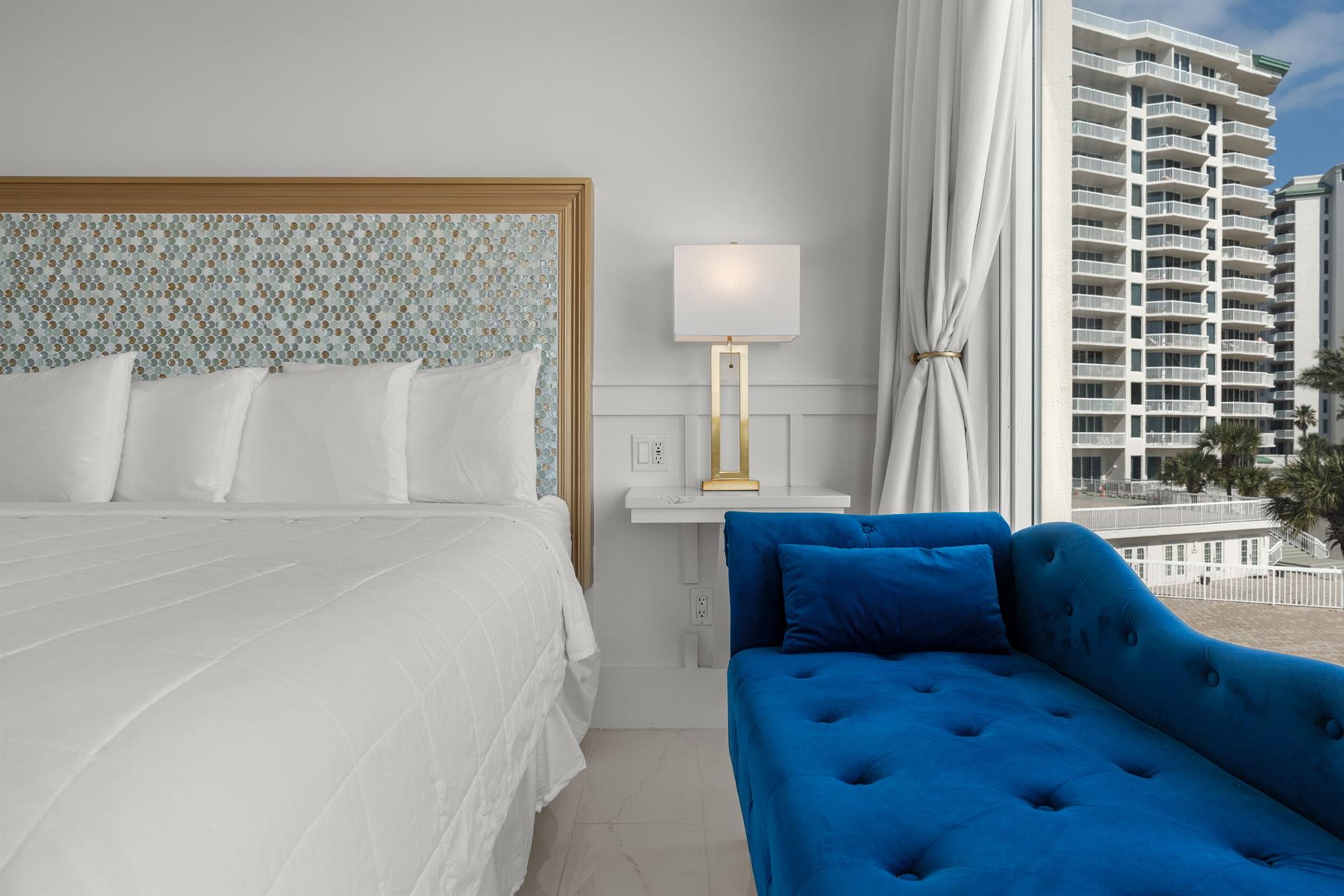 Relax in your bright, contemporary bedroom featuring a plush king bed and vibrant blue reading nook with stunning city views.