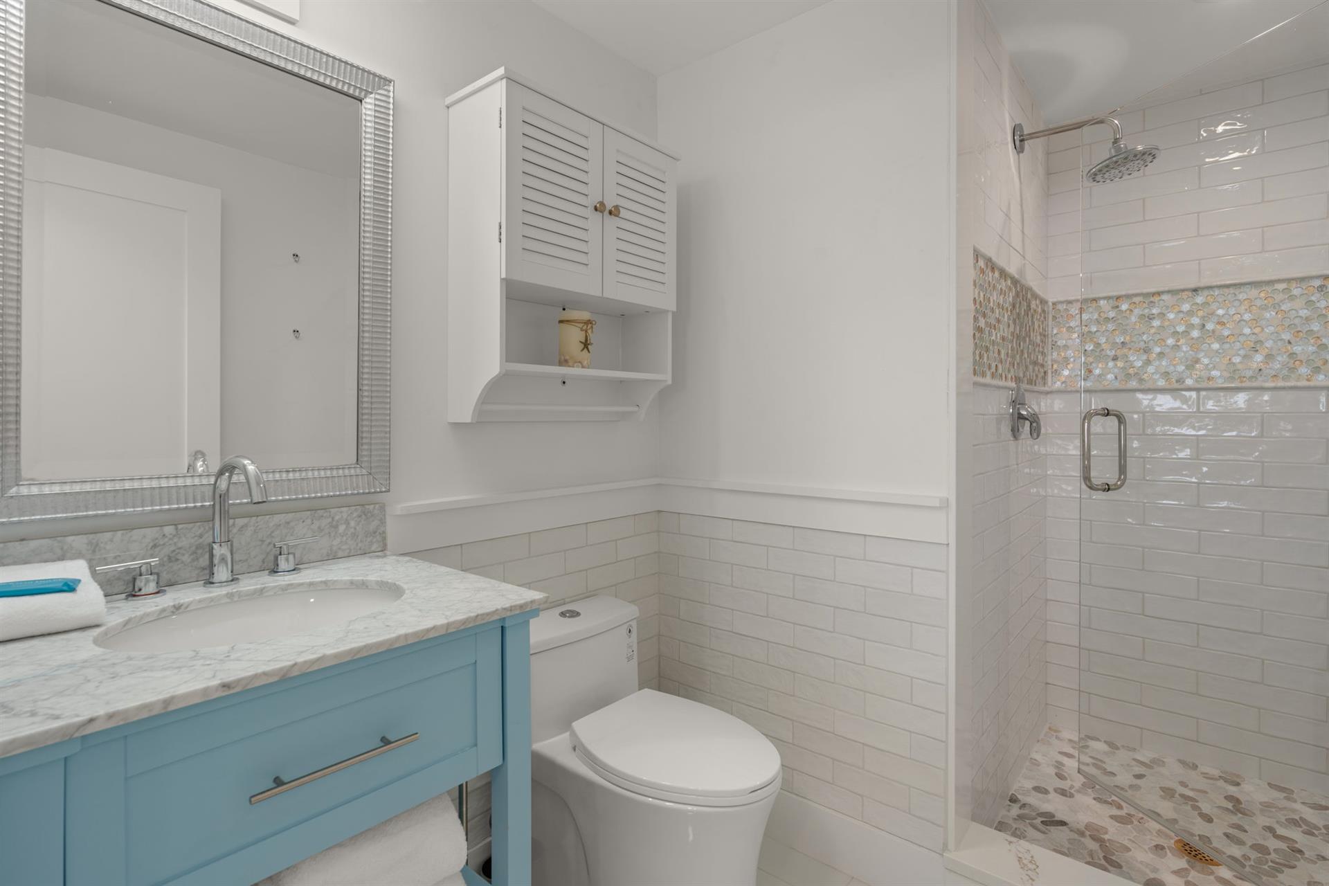 Wash up in your pristine bathroom featuring elegant subway tile, a spacious walkin shower, and charming coastal blue vanity.