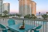 Beachfront balcony with colorful Adirondack chairs, wine setup, and views of sand, palm trees, and coastal highrises.