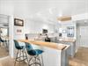 The modern kitchen features sleek white cabinets, warm wood countertops, and stylish turquoise bar seating