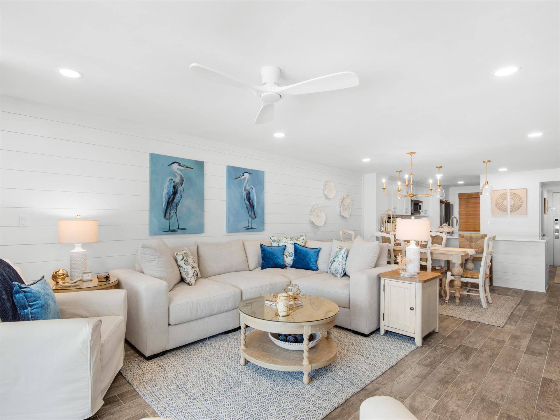 Relax in your bright, coastalinspired living space featuring plush sectional seating, charming heron artwork, and an open layout flowing into the dining area.