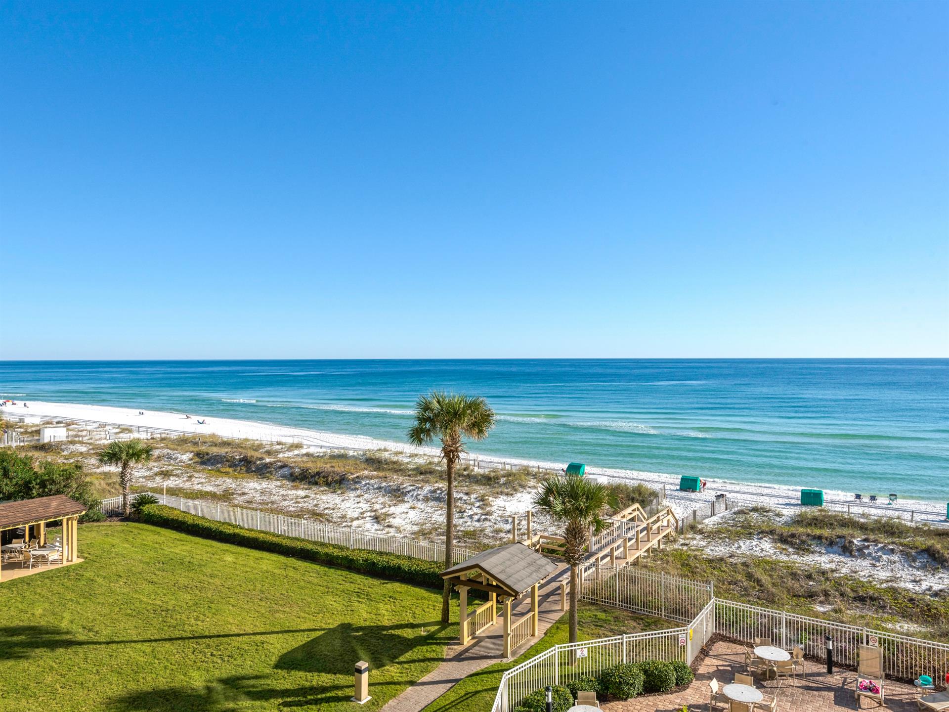 Pristine white sand beach stretches along emerald Gulf waters under endless blue skies, with convenient boardwalk access.