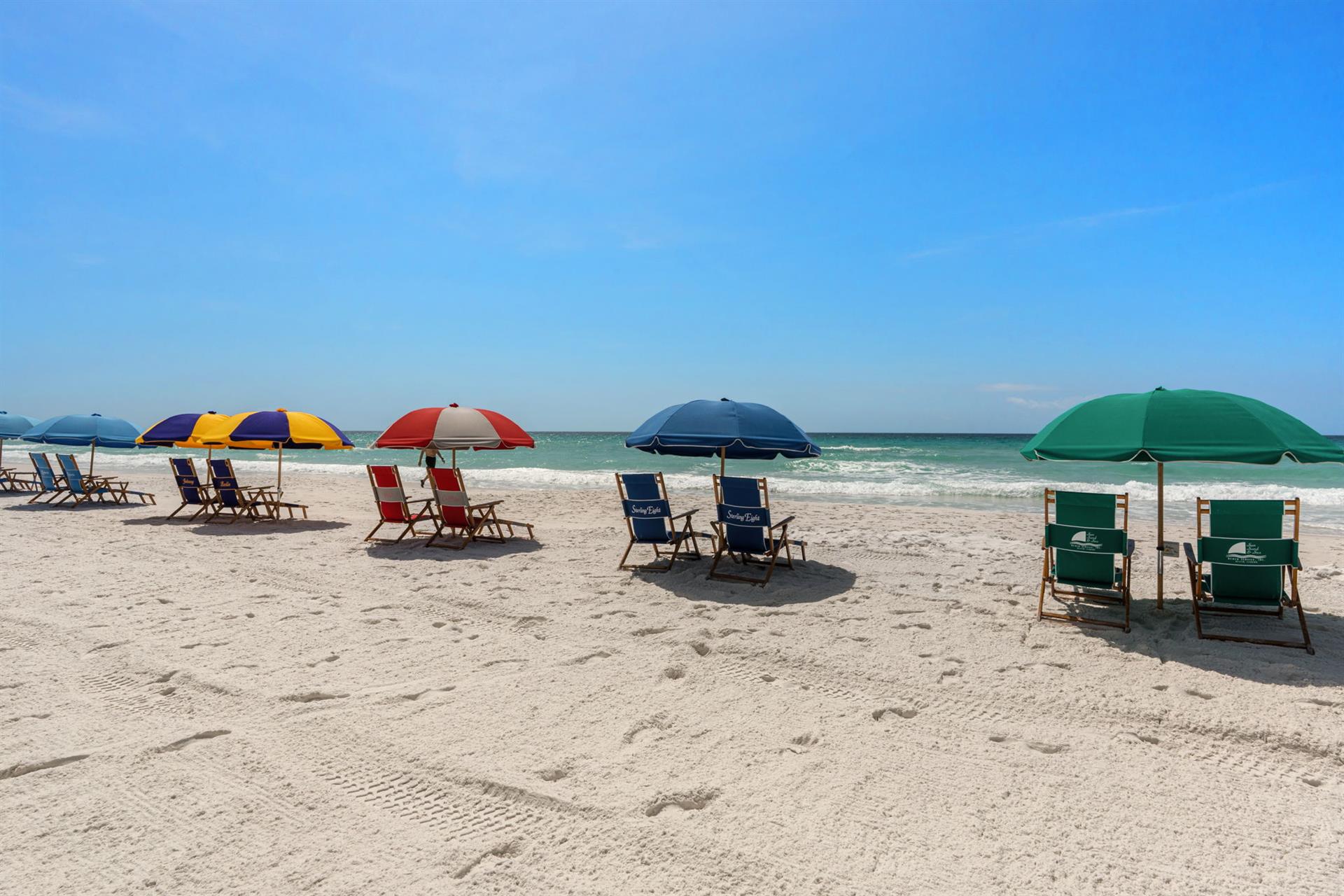 Sandy beach with colorful umbrellas and chairs set up along the pristine waterfront.