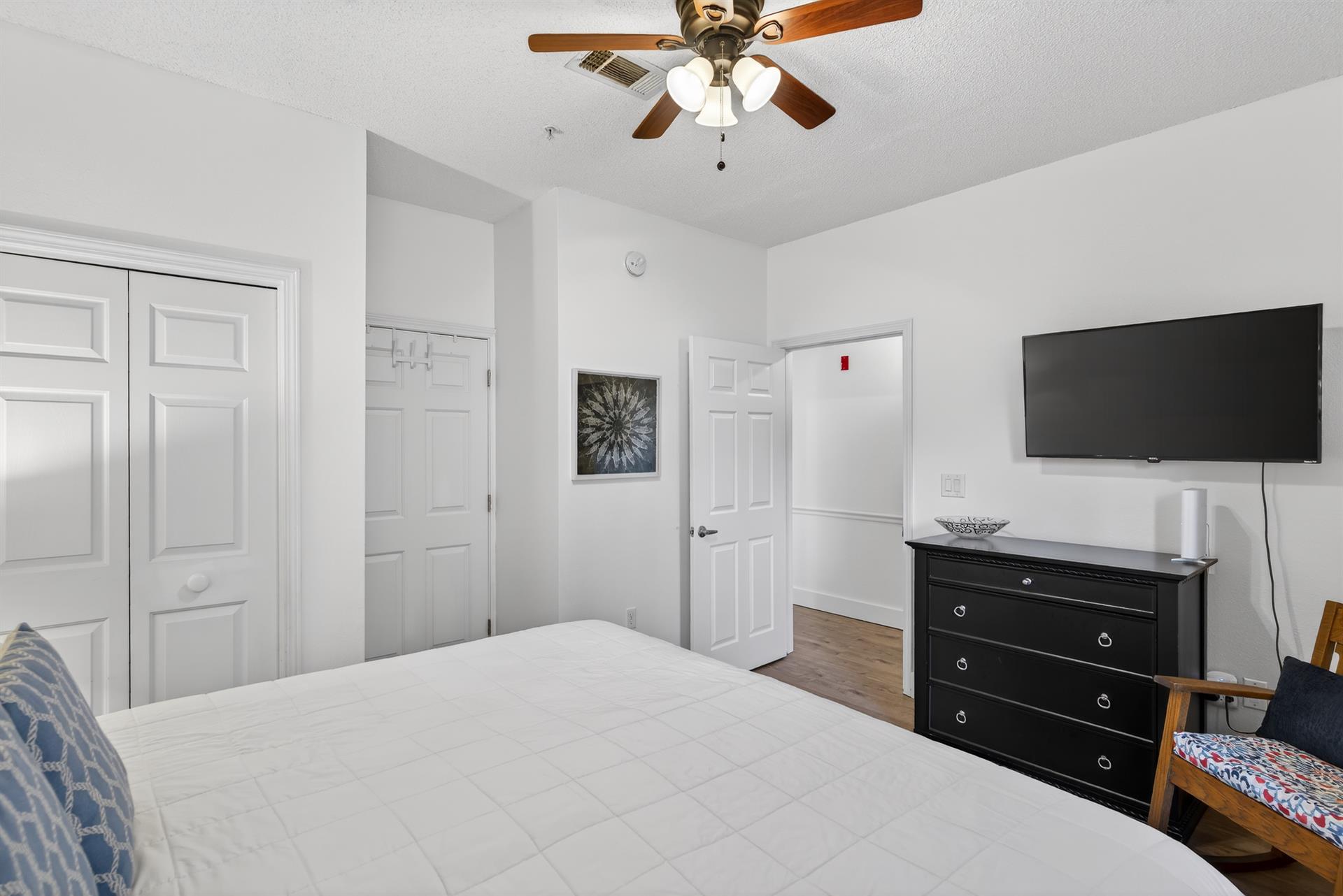 Your serene bedroom features a ceiling fan, flatscreen TV, and ample storage in the elegant black dresser for a comfortable stay.