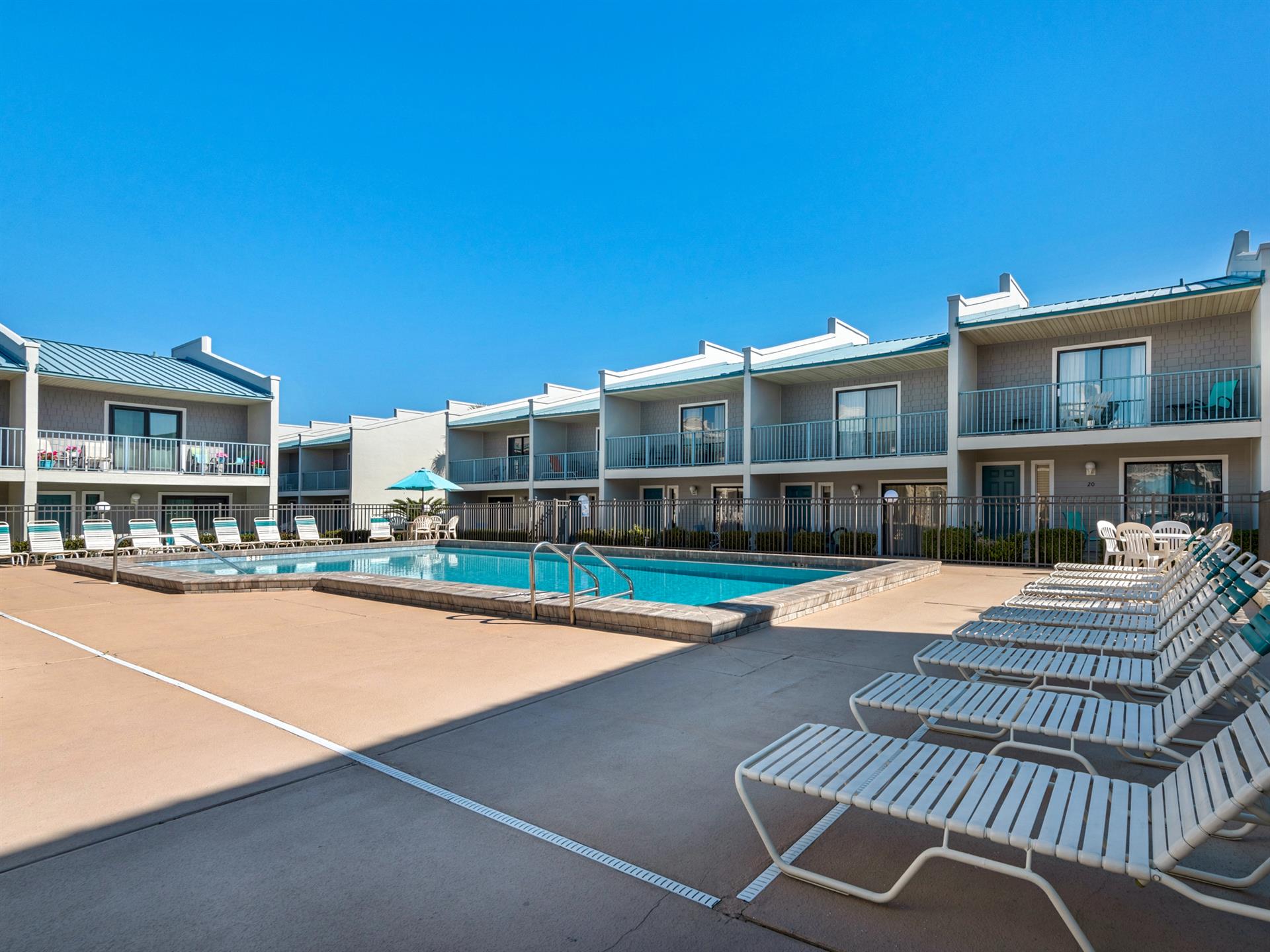 Multistory vacation rental complex featuring a central swimming pool surrounded by modern accommodations with balconies and outdoor seating areas.