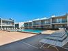 Multistory vacation rental complex featuring a central swimming pool surrounded by modern accommodations with balconies and outdoor seating areas.