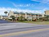The Gulf Winds East resort stands prominently along the coastal road, featuring tropical landscaping and blue metal roofing that complements the scenic surroundings.