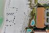 Aerial view of a beachfront property featuring two swimming pools, direct beach access with pristine white sand, and proximity to calm, turquoise waters ideal for relaxation.