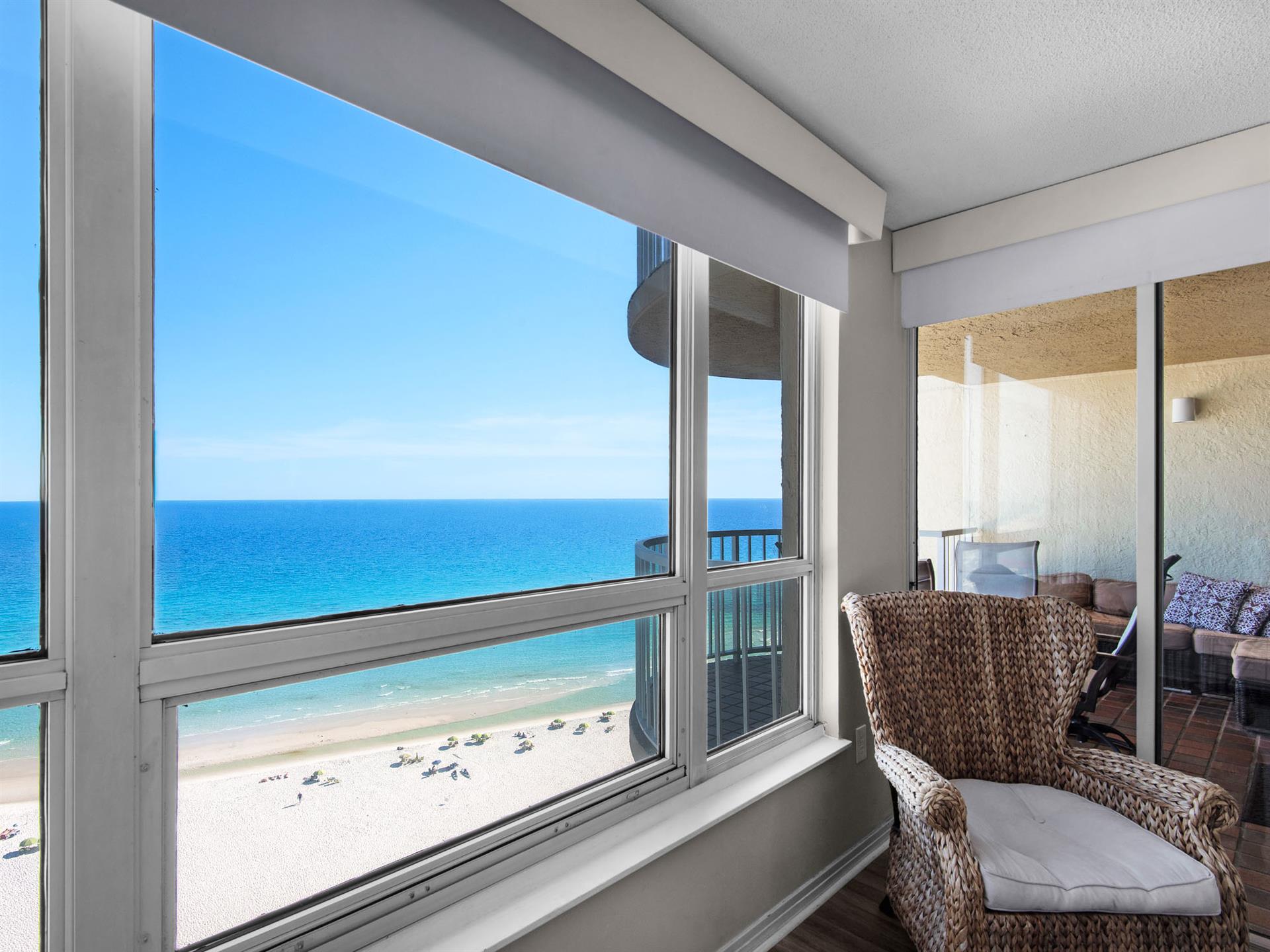 Stunning beachfront views frame your private sanctuary, where turquoise waves meet soft sand and a cozy woven chair invites you to relax
