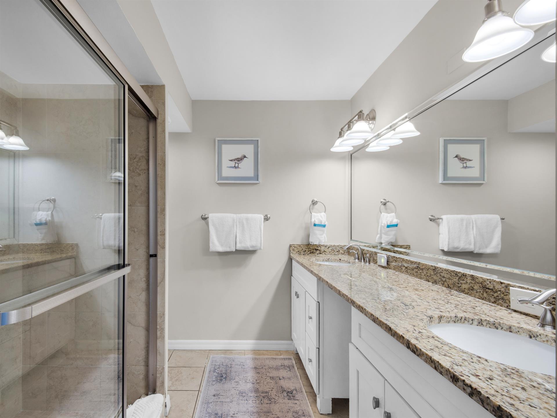 Coastalinspired bathroom featuring a walkin shower and dual vanity. Soft lighting and fresh towels await after your day exploring.