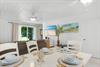 Picture yourself at this dining table set for a meal, with coastal artwork adorning the walls and natural light streaming through to the living area beyond.