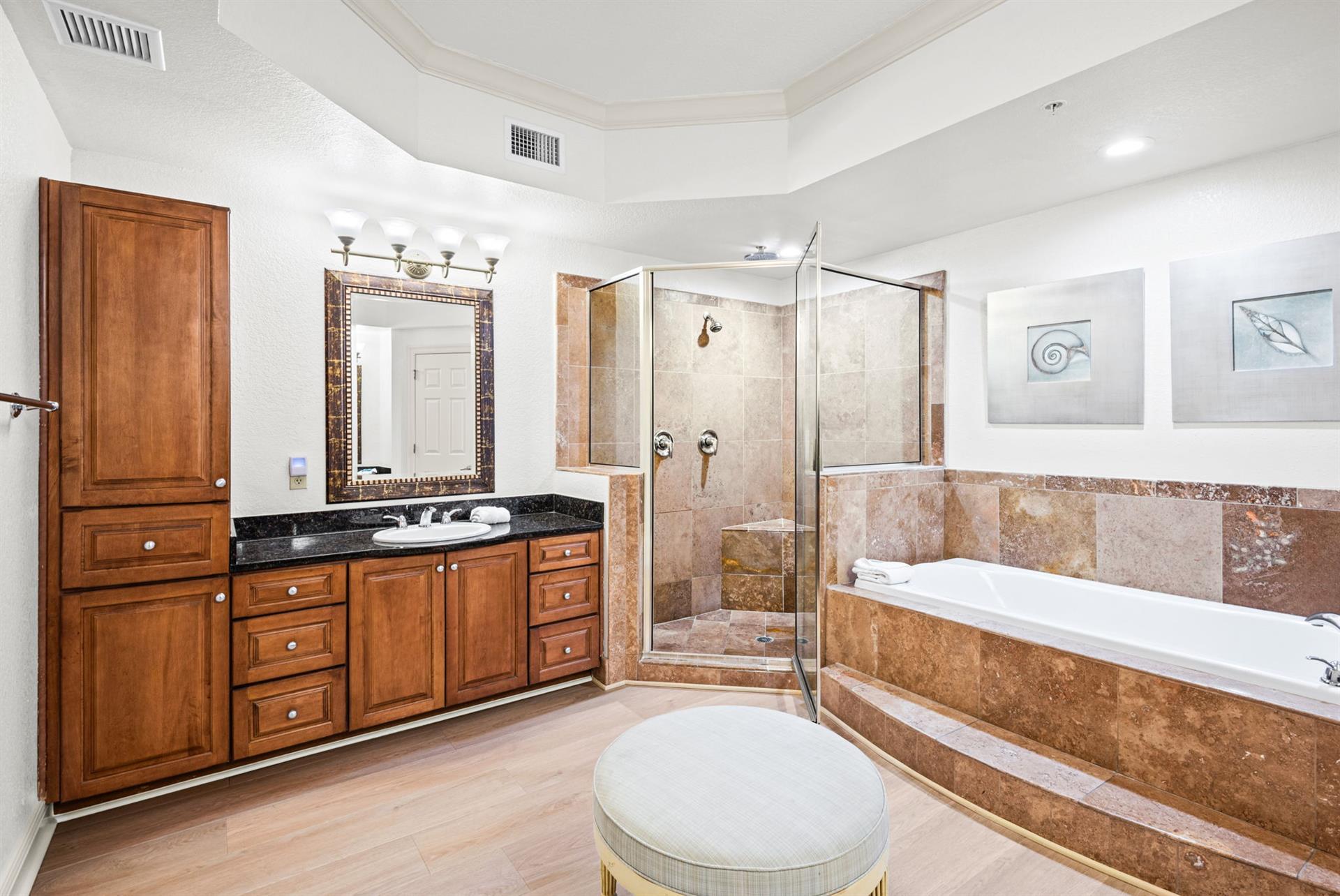 The primary bathroom offers a deep soaking tub, spacious walkin shower with dual showerheads, elegant stone tile, and abundant storage in rich wood cabinetry.