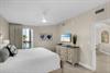 The primary bedroom features a plush bed, beachy artwork, and a TV perfect for unwinding