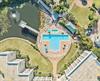 Aerial view showcasing the resorts distinctive crossshaped pool, surrounded by lush gardens, waterfront access, and modern accommodations—a tranquil retreat nestled between green lawns and natural w