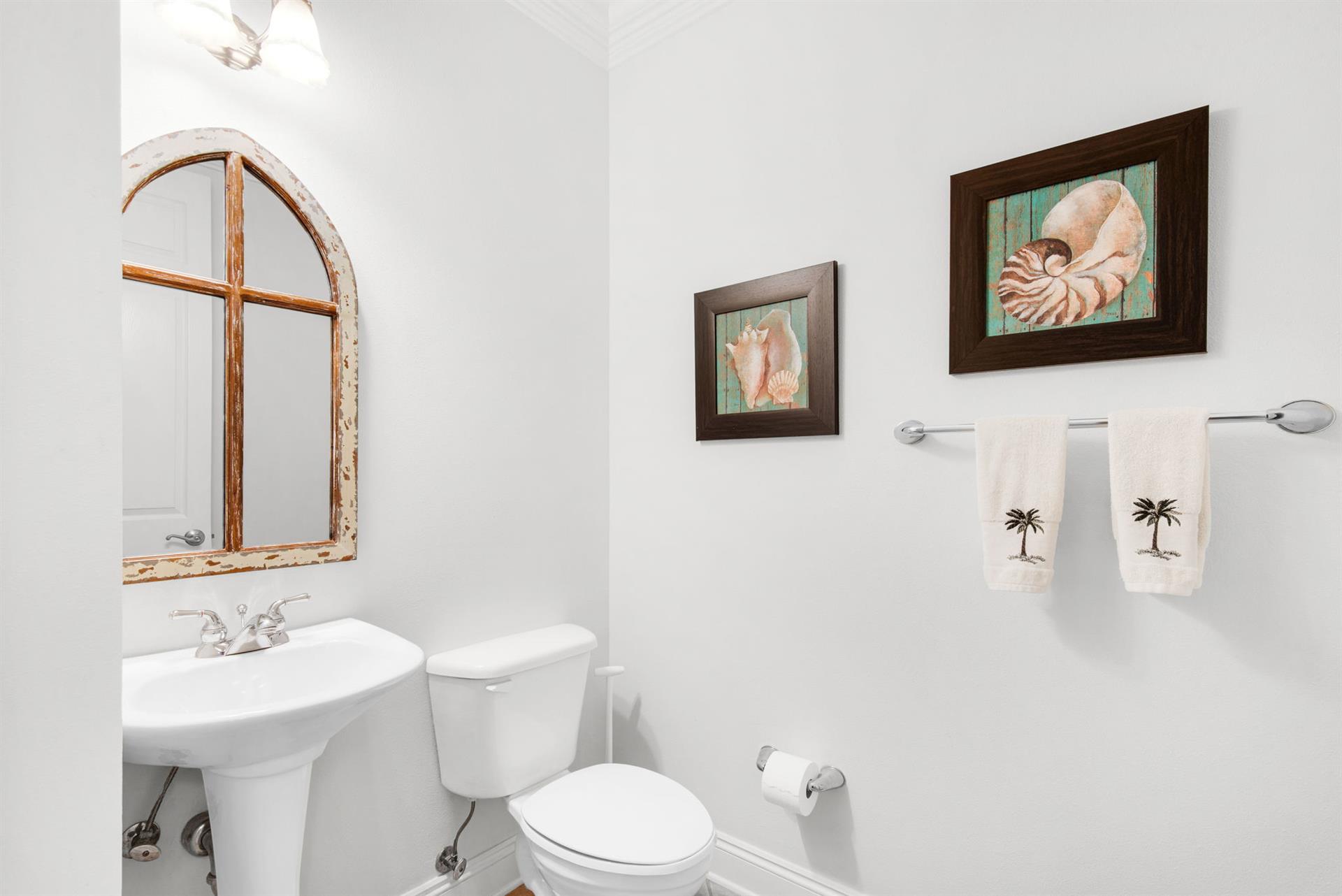 The powder room features coastal accents, soft lighting, and a charming arched mirror.