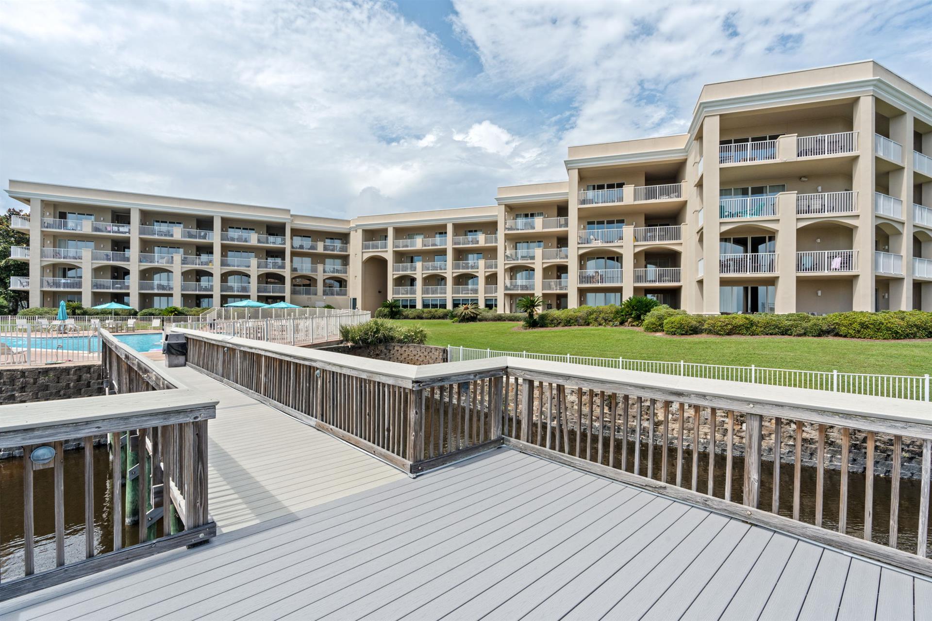 Threestory property features tiered architecture with multiple balconies, manicured lawn, swimming pool, and waterfront access via private boardwalks.