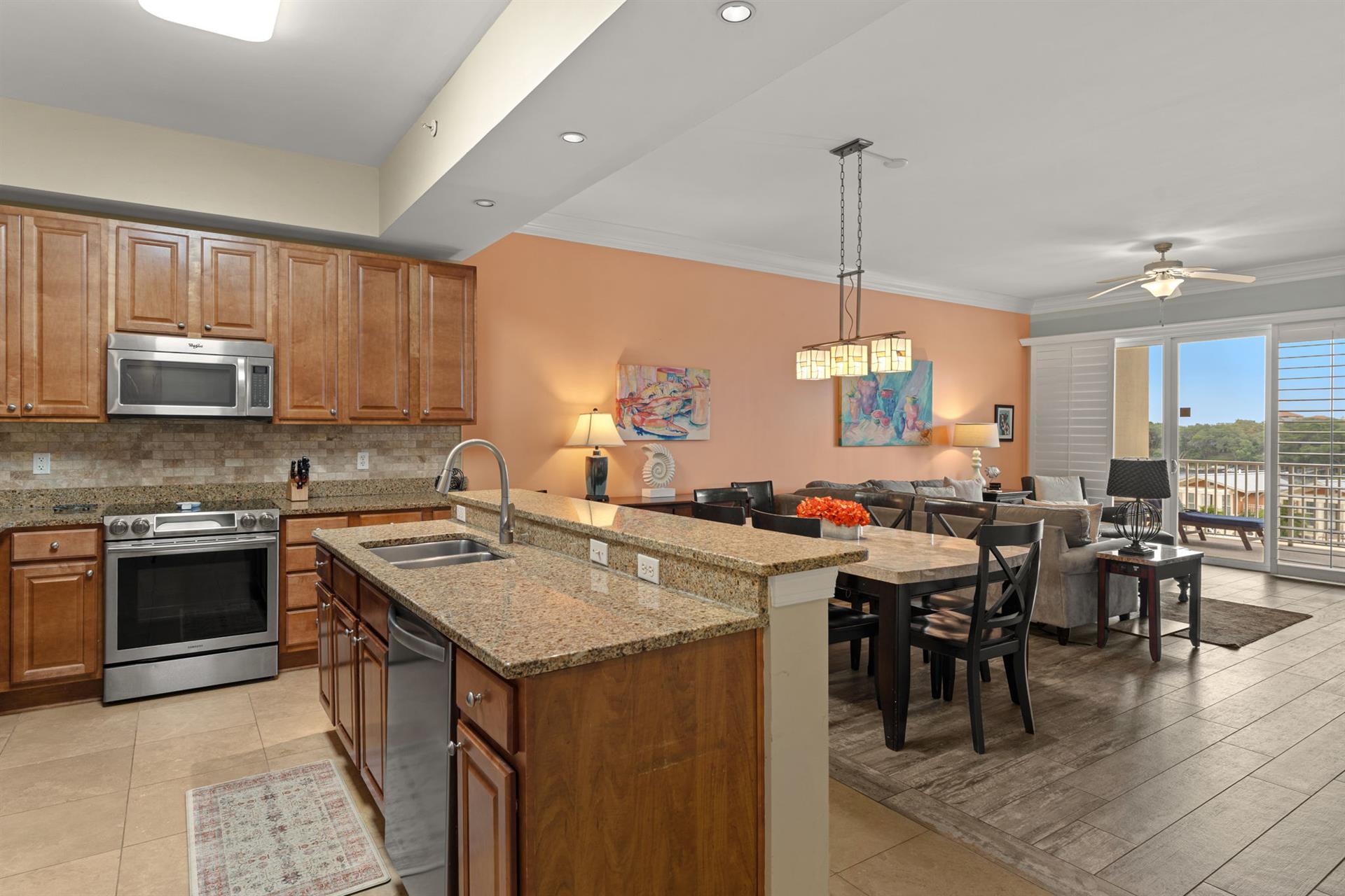 This openconcept kitchen and living space invites relaxed gatherings with granite countertops, stainless appliances, and natural light flowing in from the balcony doors.