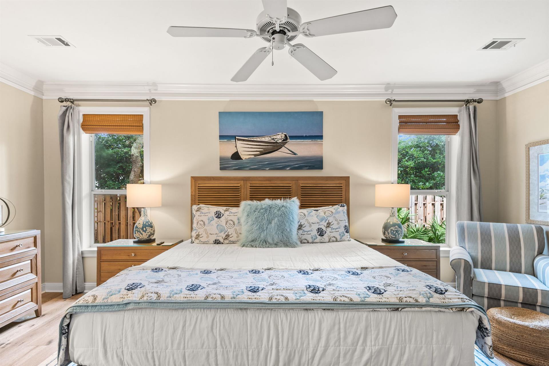 Sink into this coastalinspired primary bed and unwind beneath the gentle breeze of the ceiling fan as soft morning light filters through your windows.