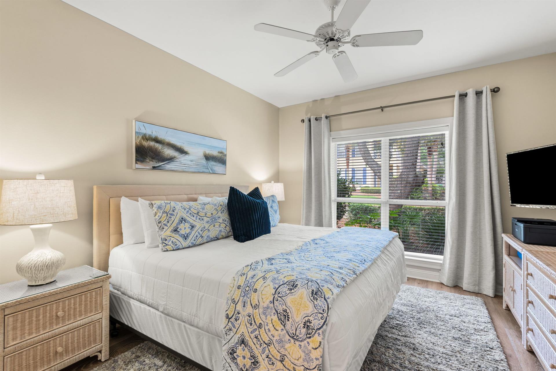 Unwind in your serene bedroom with plush bedding, coastal artwork, and a garden view beyond the window.
