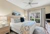 Unwind in your serene bedroom with plush bedding, coastal artwork, and a garden view beyond the window.