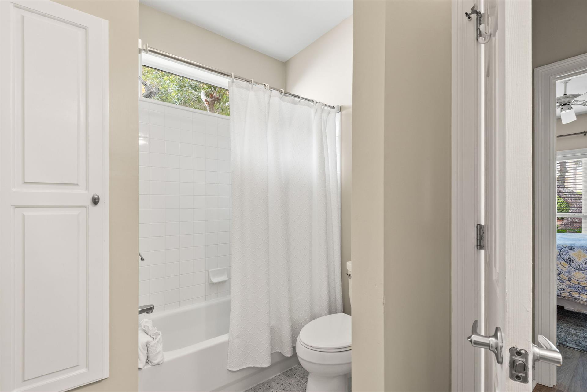The bathroom features a refreshing showertub combo with crisp white tiling, soft natural light from above.