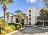 A welcoming property nestled among lush palm trees and manicured landscaping, featuring Mediterraneaninspired architecture with a covered entrance and multiple balconies overlooking beautifully maint