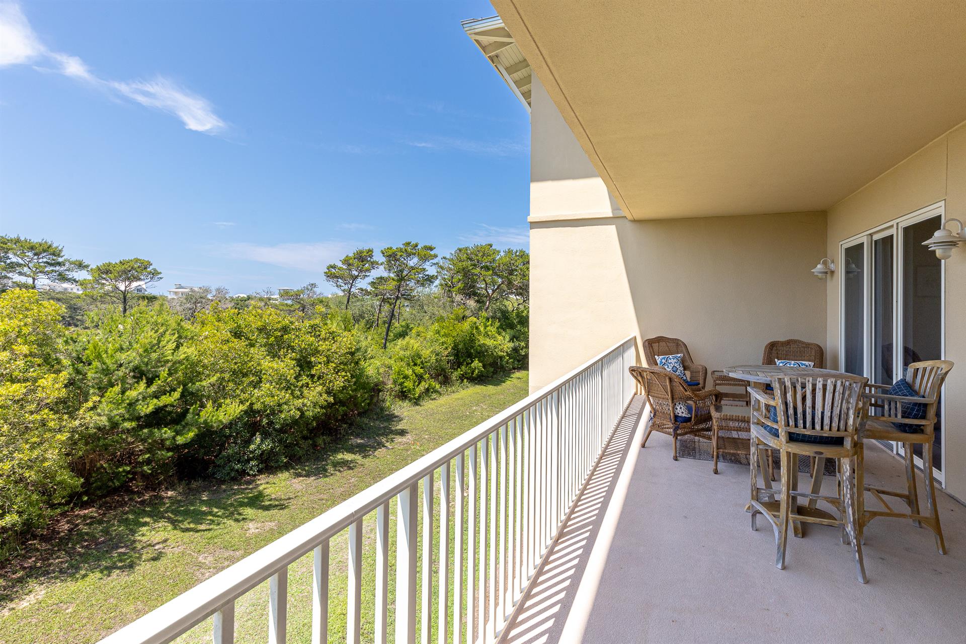 A spacious outdoor terrace overlooks lush coastal greenery under clear blue skies, offering the perfect spot to dine al fresco or simply unwind.