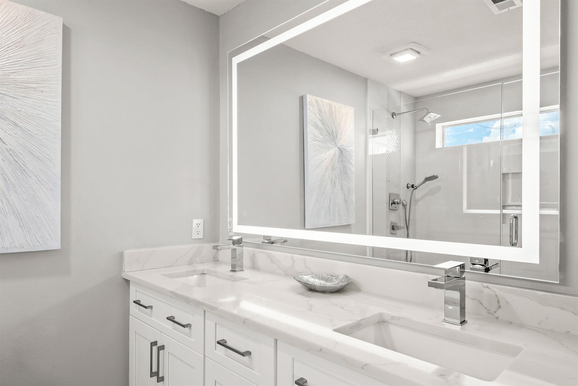 Bathroom 1 with dual sinks set in beautiful marble countertops, a bright LED mirror, and a sleek glassenclosed shower.
