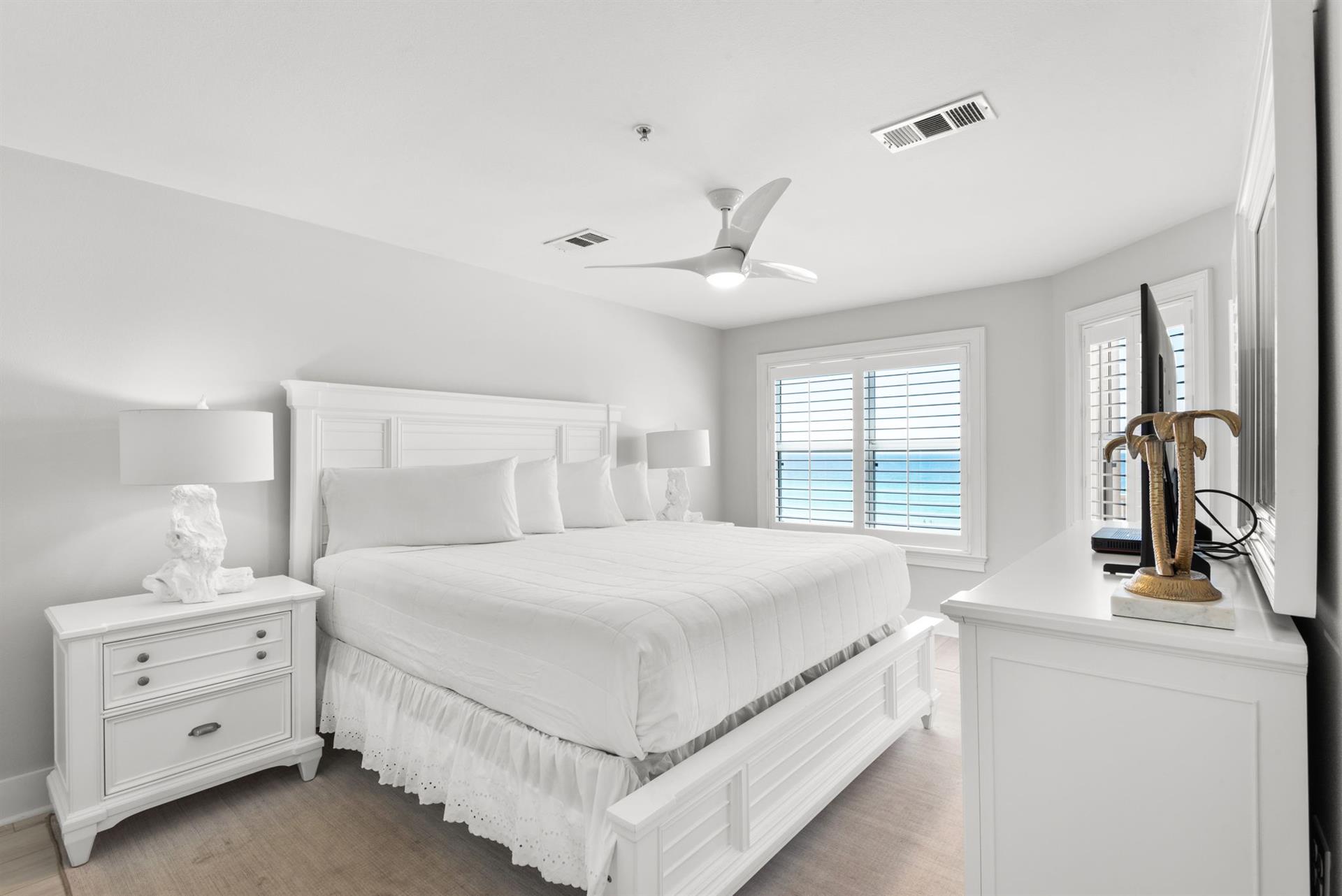 Drift off in this serene coastal bedroom with crisp linens, gentle sea breezes from the ceiling fan, and peaceful ocean glimpses through plantation shutters.