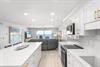 Bright, modern kitchen with sleek white cabinetry and gold hardware opens to stunning ocean views. Sunlight streams through the balcony doors, perfect for coastal living.